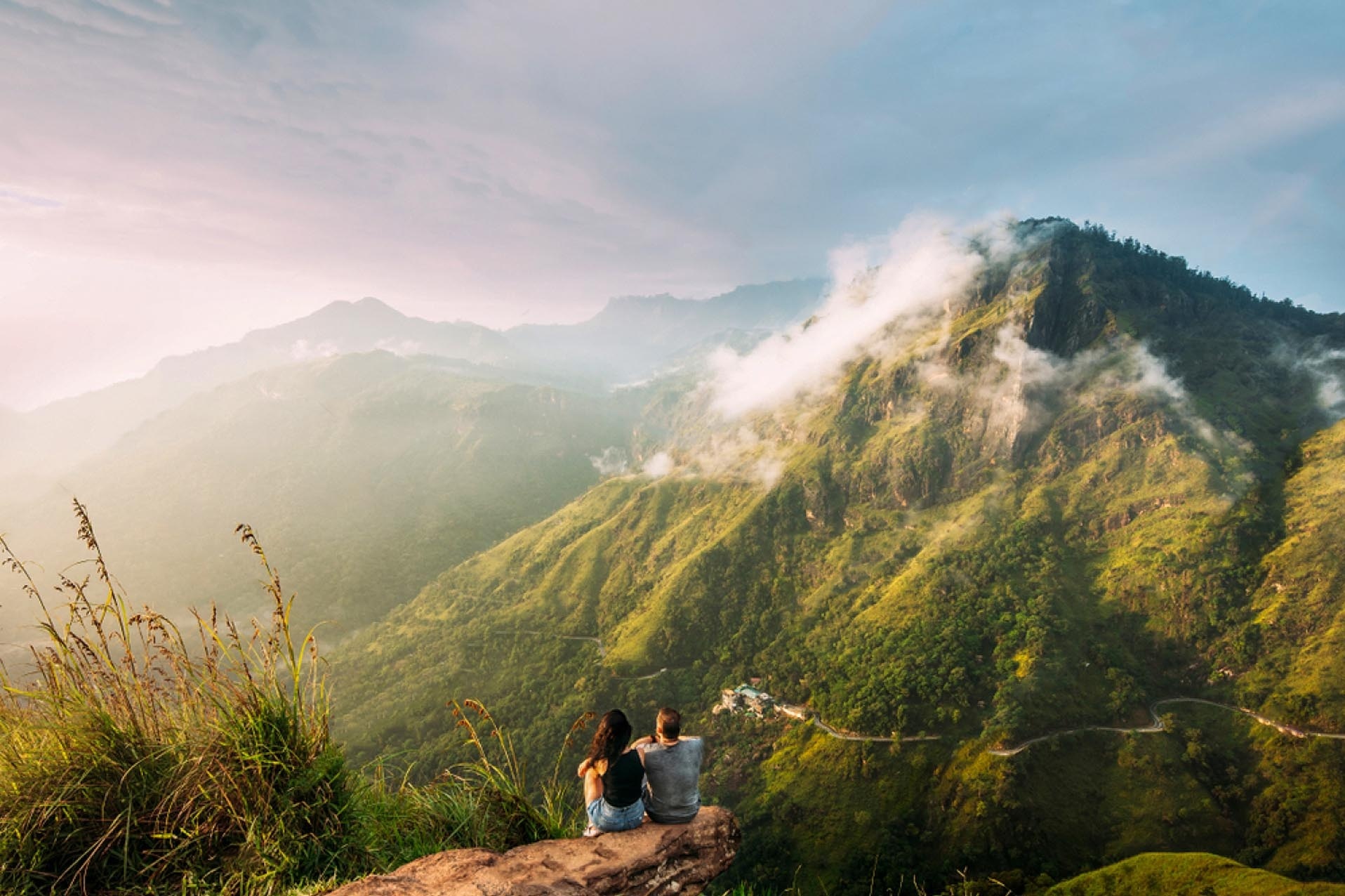 Zwei Personen sitzen auf einem Felsen mit Blick auf eine Berg.