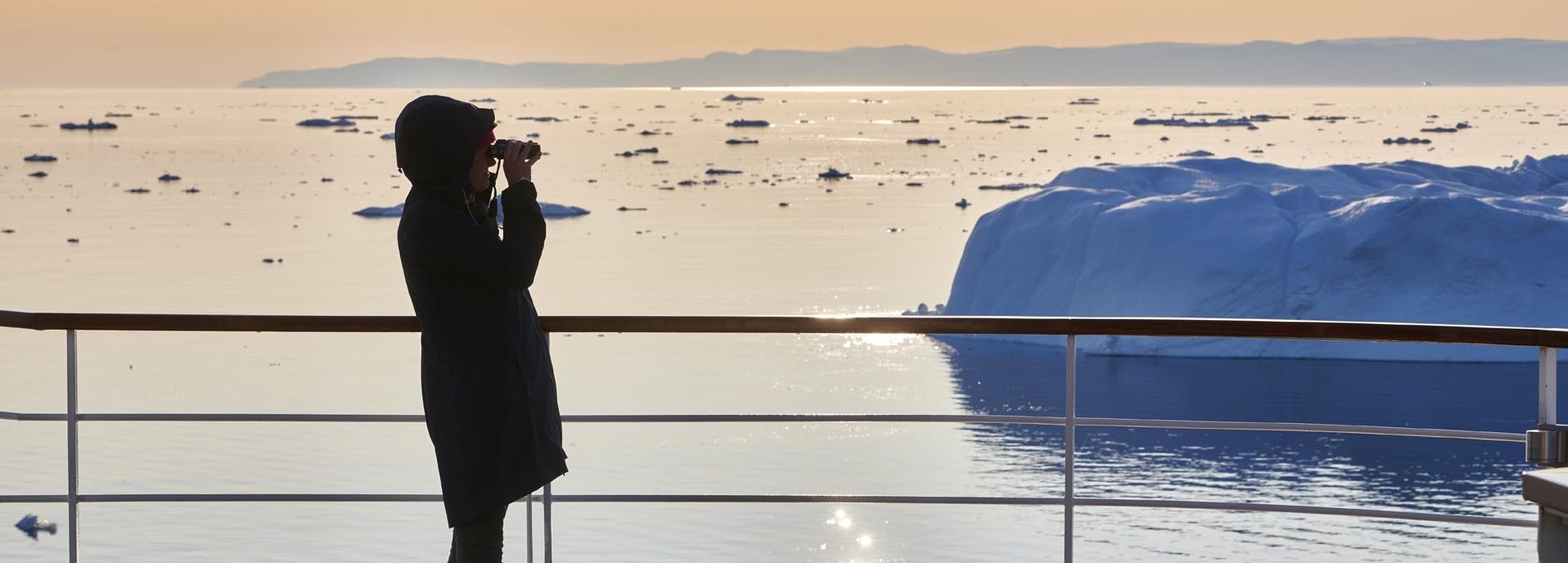 Eine Frau steht mit einem Fernglas auf dem Deck eines Schiffes.