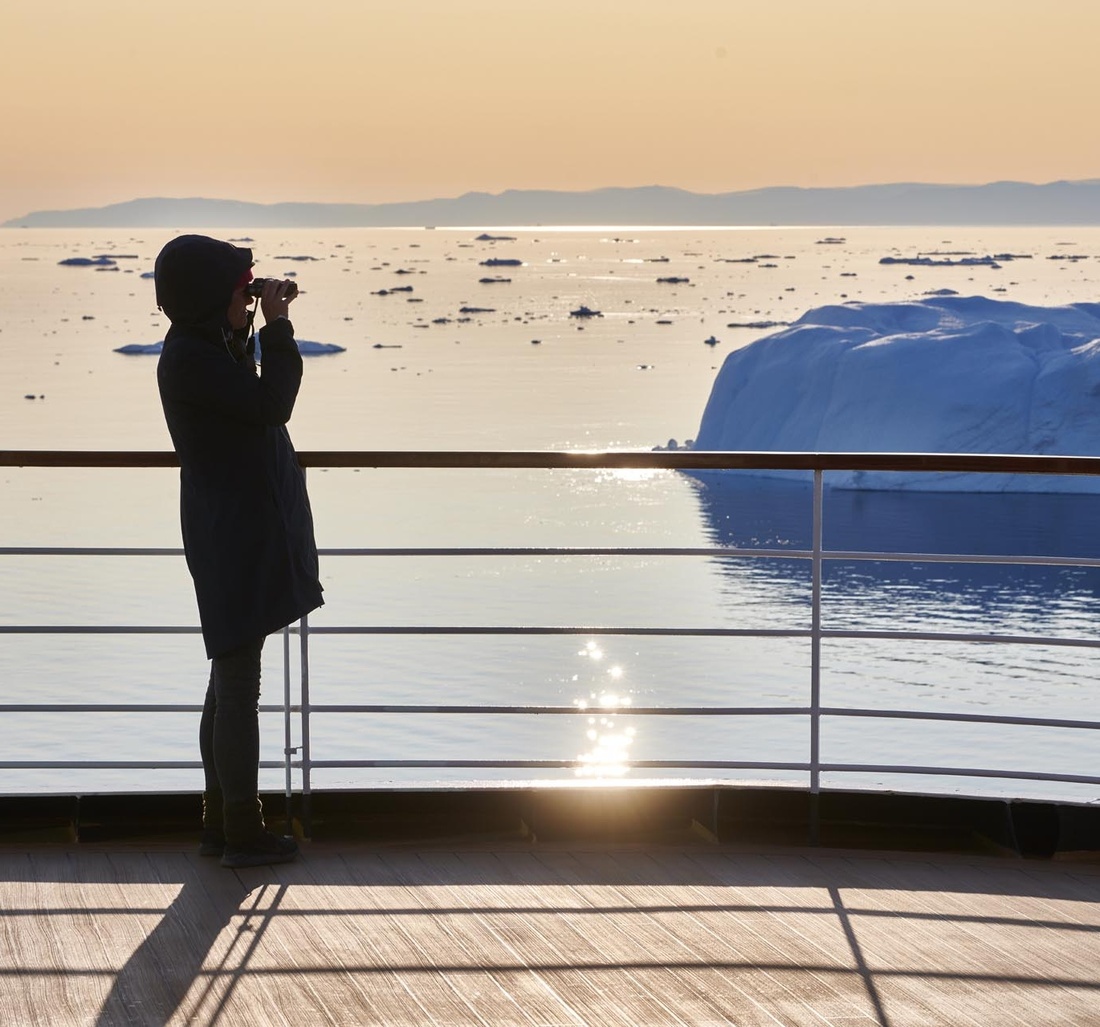Eine Frau steht mit einem Fernglas auf dem Deck eines Schiffes.