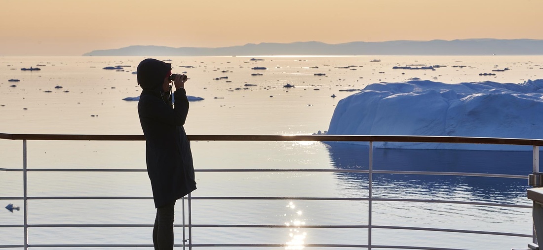 Eine Frau steht mit einem Fernglas auf dem Deck eines Schiffes.