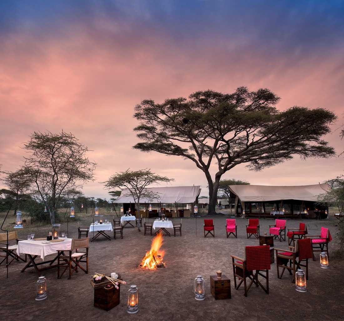 Tische und Stühlen stehen um ein Lagerfeuer herum.