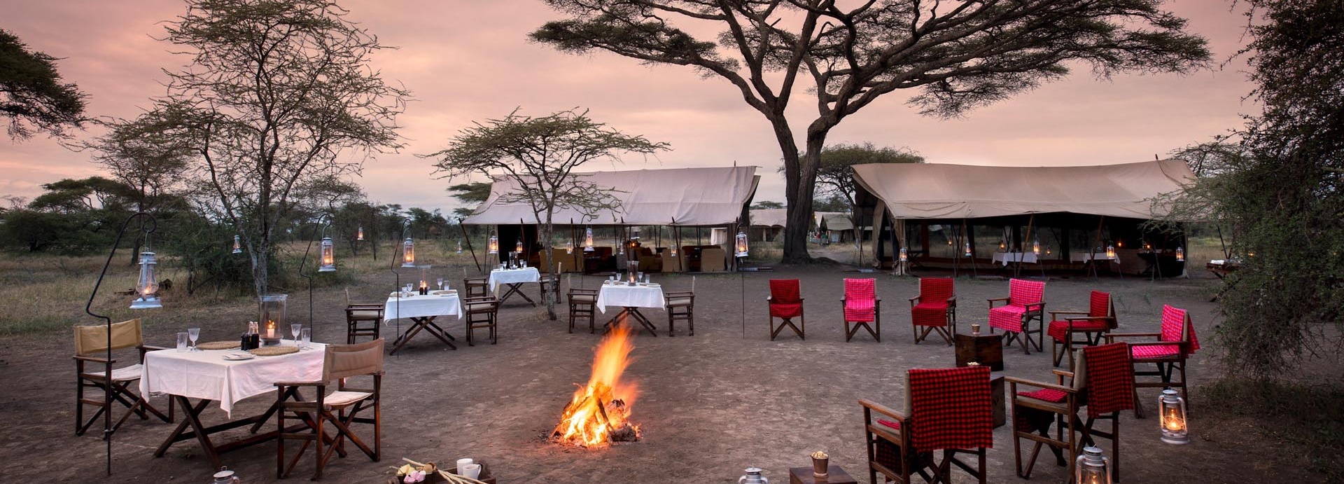 Tische und Stühlen stehen um ein Lagerfeuer herum.