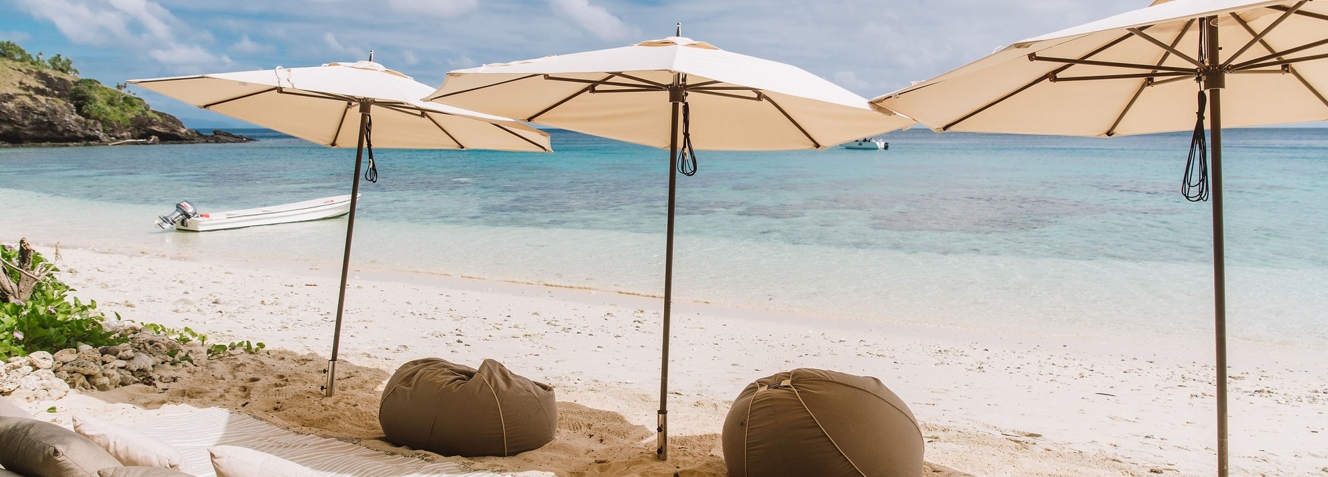 Kissen und Sitzsäcke am Strand unter Sonnenschirmen.