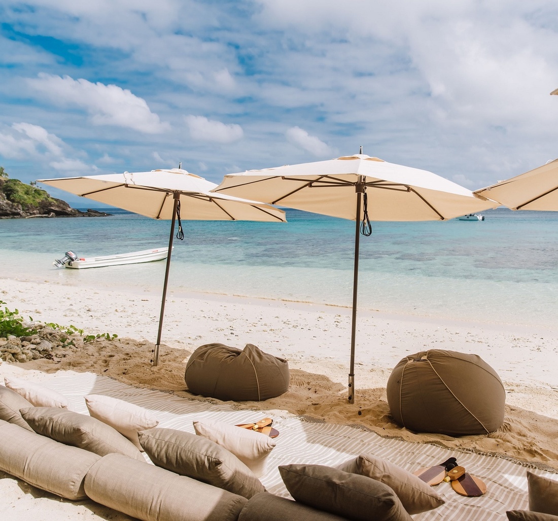 Kissen und Sitzsäcke am Strand unter Sonnenschirmen.