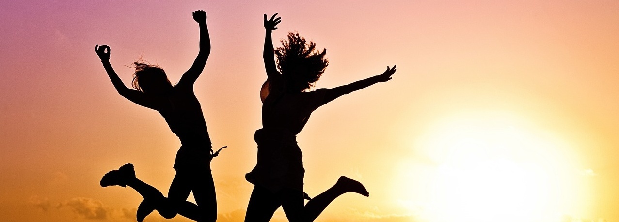 Zwei Frauen springen in die Luft während eines Sonnenunterganges.