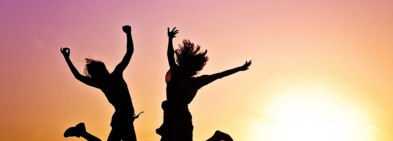 Zwei Frauen springen in die Luft während eines Sonnenunterganges.