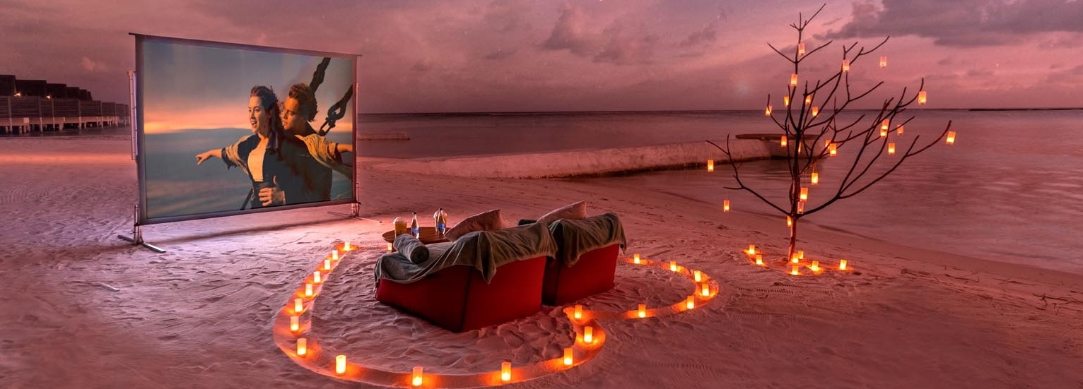 Auf einem Strand stehen zwei Sessel und eine Leinwand auf dieser der Film Titanic läuft.