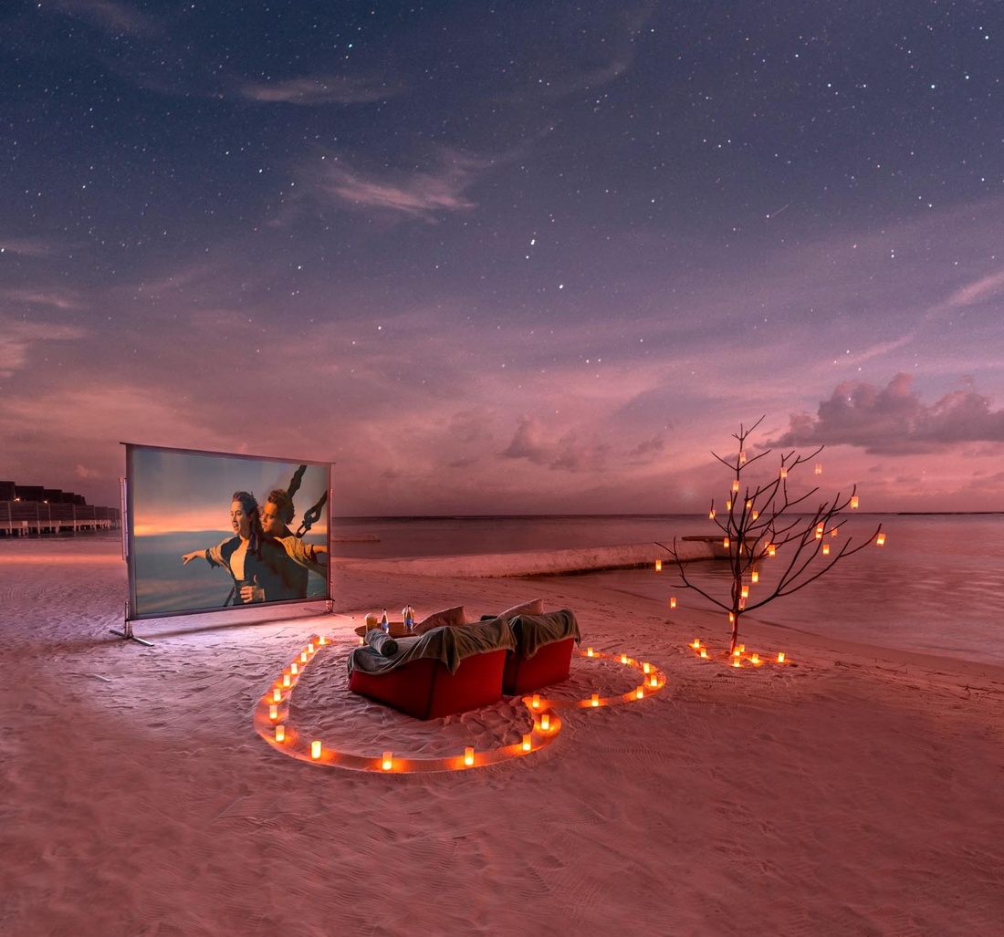 Auf einem Strand stehen zwei Sessel und eine Leinwand auf dieser der Film Titanic läuft.
