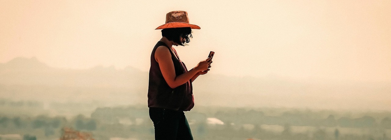 Frau mit Hut und Mobiltelefon auf einem Berg