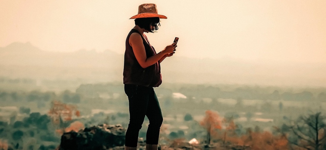 Frau mit Hut und Mobiltelefon auf einem Berg