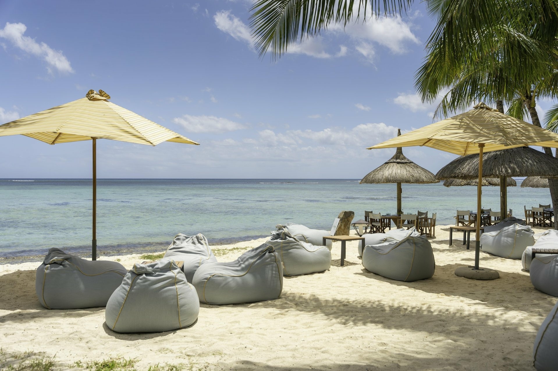 Sitzsäcke und TIsche mit Sonnenschirm unter Palmen am Strand