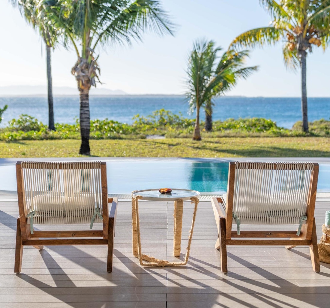 Zwei Sonnenstühle und ein kleiner Tisch stehen vor einem Pool.