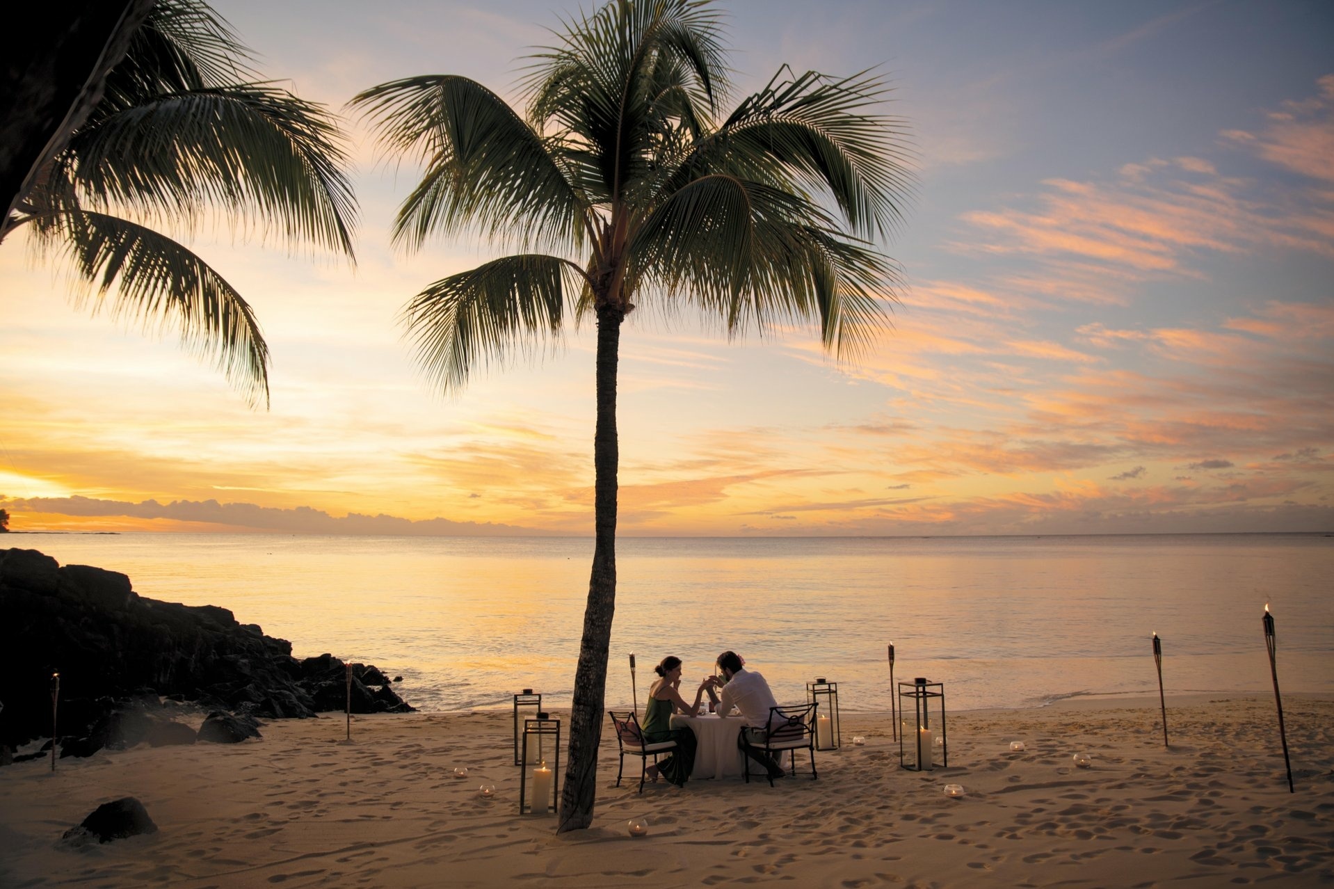 Paar beim romantischen Dinner am Strand unter Palme beim Sonnenuntergang