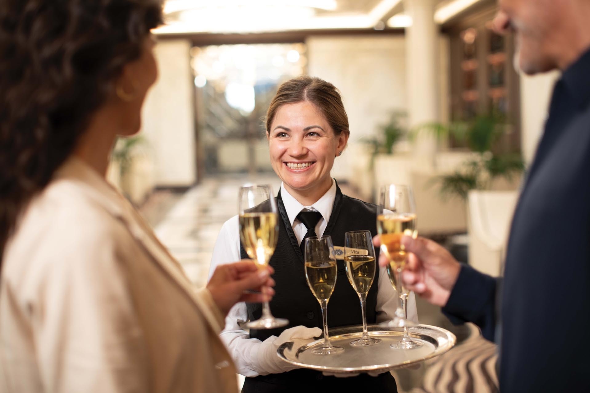 Eine Angestellte begrüßt Gäste mit einem Champagner.