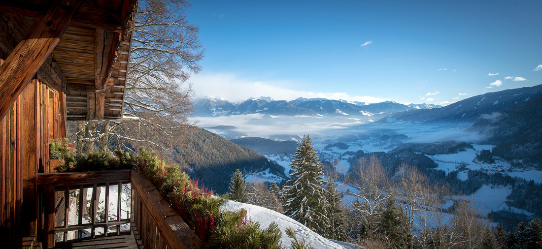 Eine Holzhütte vor einer verschneiten Bergkulisse.