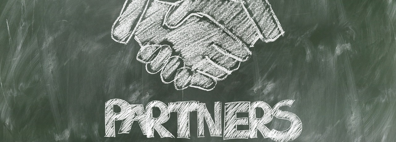 Auf einer grünen Tafel, sind mit Kreide ein Handschlag und der Schriftzug Partners gezeichnet.