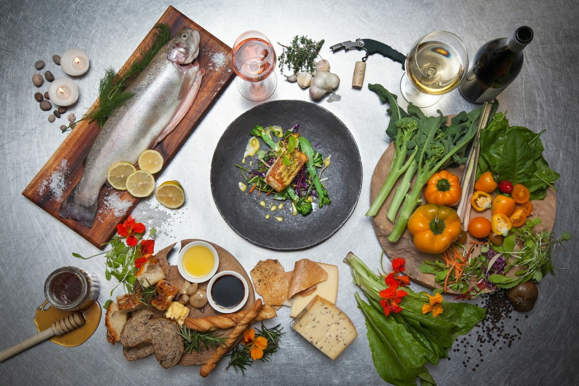 Ein Tisch mit zwei Wein Gläsern, Fisch, Gemüse, Brot und andere Köstlichkeiten darauf.