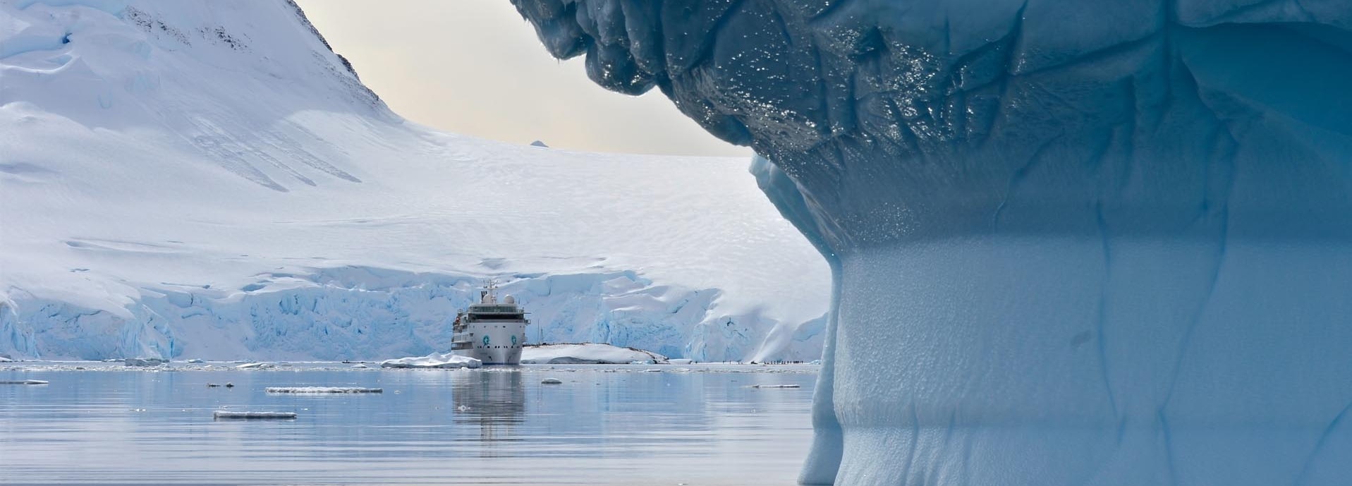 Ein Schiff fährt vor einem großen Eisberg.