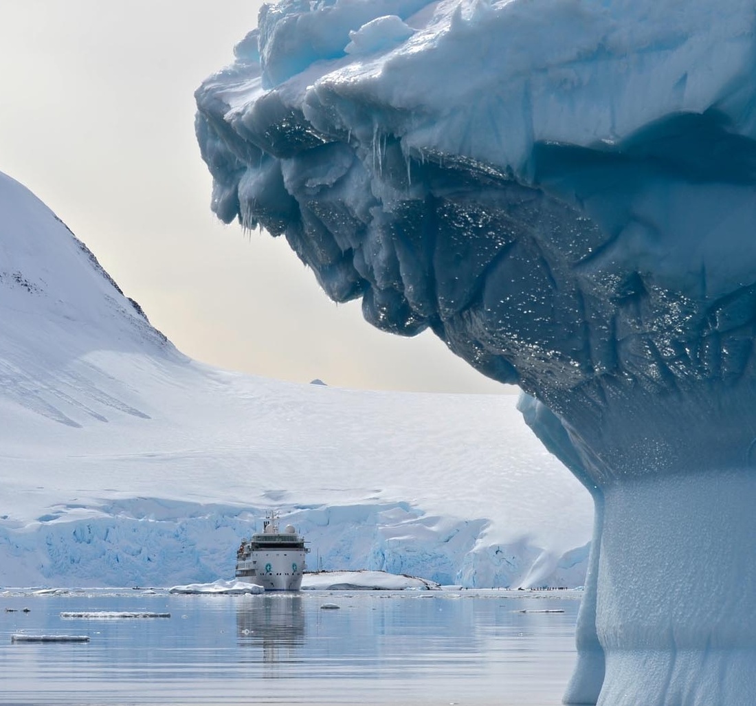 Ein Schiff fährt vor einem großen Eisberg.