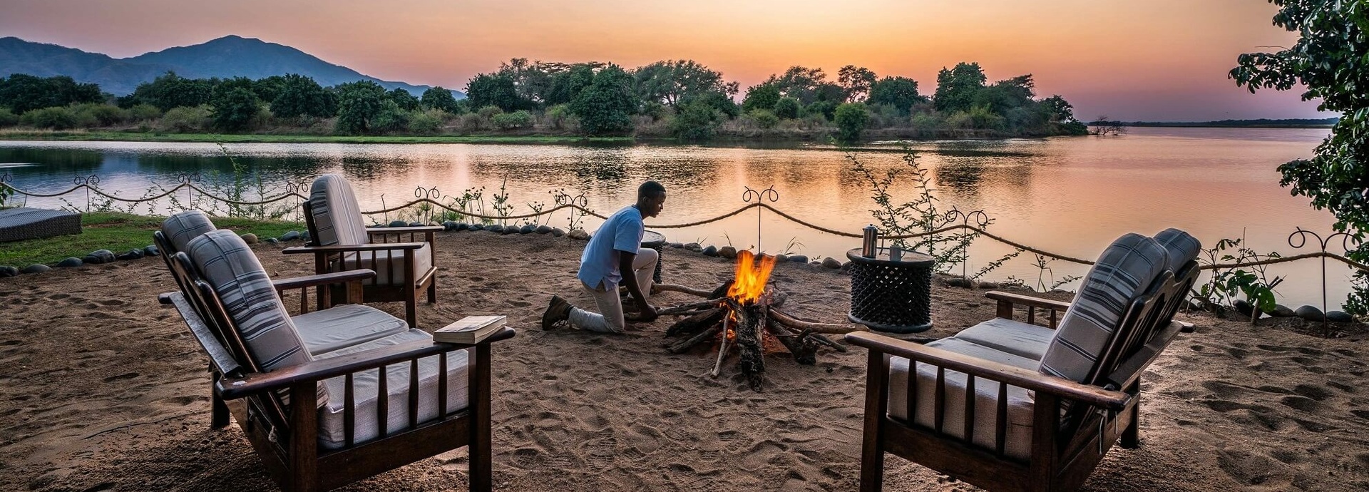 Ein Mann kniet vor einem Lagerfeuer.