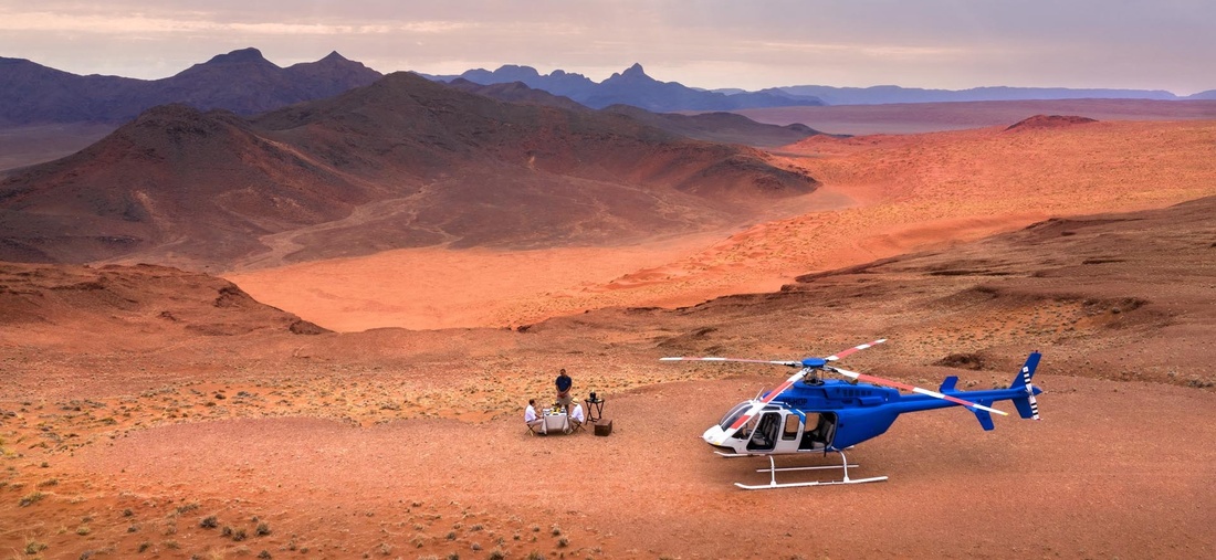 Ein blauer Helikopter steht, in der Wüste, neben drei Personen.