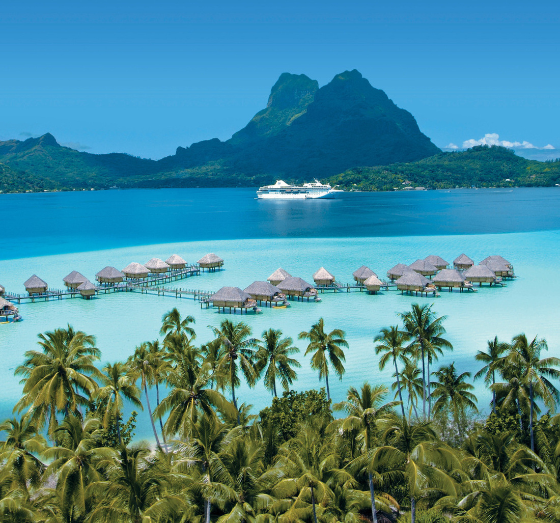 Ein Holzsteg führt zu mehreren Unterkünften im Wasser.