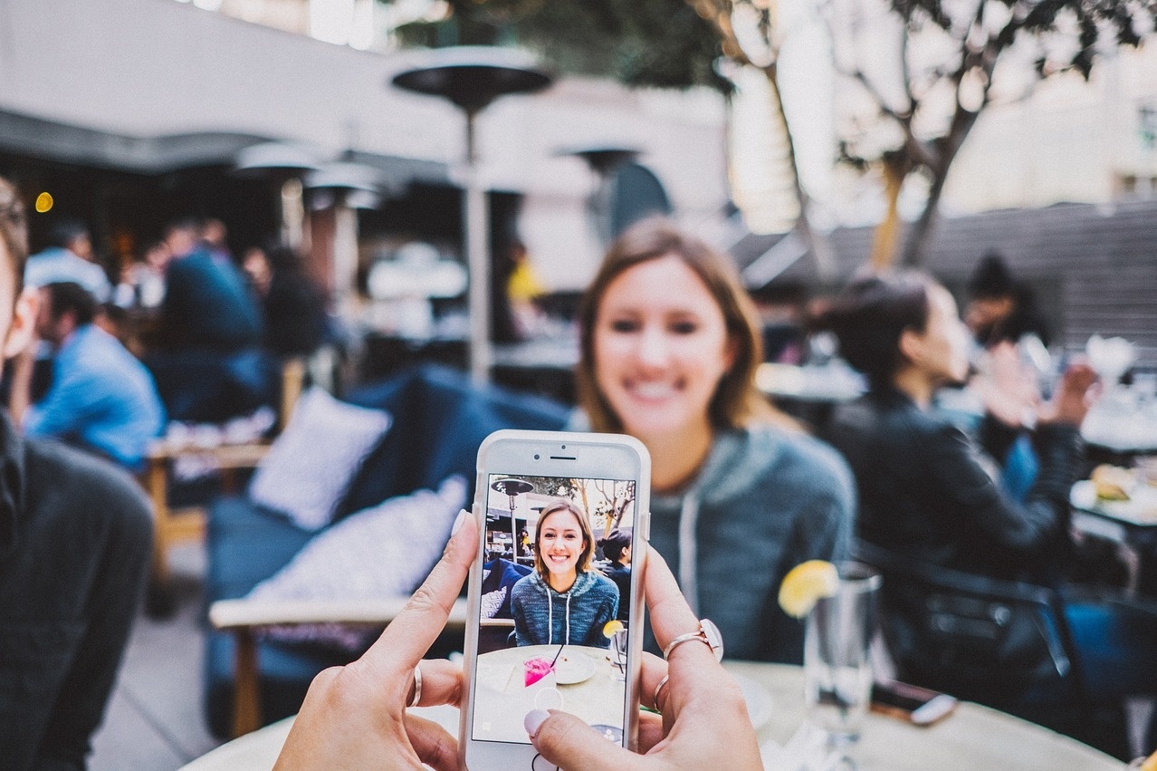 Frau macht Foto von einer Freundin mit Mobiltelefon